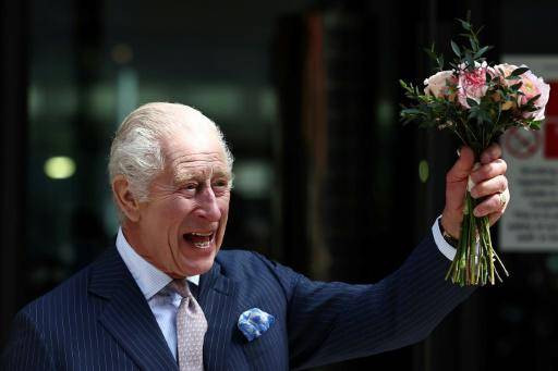 El rey Carlos III sonríe con un ramo de flores en la mano al saludar a los curiosos durante una visita a la sección oncológica de un hospital, el 30 de abril de 2024 en Londres