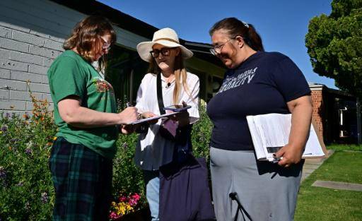 Las voluntarias Liz Grumbach (C) y Patricia Jones se reúnen con Lucy Meyer (I), que firma una petición frente a su casa en Phoenix, Arizona, el 13 de abril de 2024
