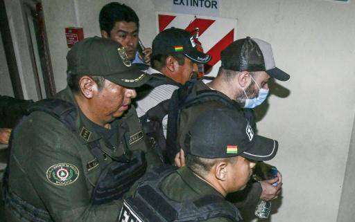 Tres policías trasladan al argentino Fernando Cerimedo (con mascarilla) desde el palacio de justicia a una cárcel de Santa Cruz, el 21 de agosto de 2026 en esa ciudad de Bolivia