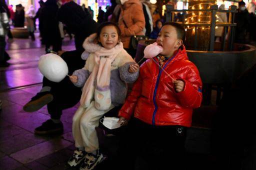 Dos niños comen dulces en una calle comercial de Pekín durante las celebraciones del Año Nuevo Lunar, el 25 de enero de 2023 en la capital china