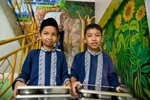 Dos alumnos portan unas bandejas de comida proporcionadas por el programa gratuito del gobierno de Indonesia el 30 de octubre de 2025 en una escuela en Banda Aceh