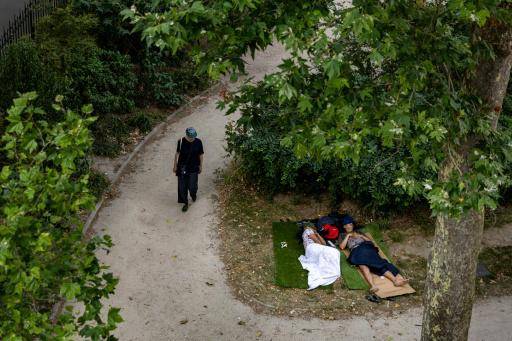 Una persona camina junto a dos personas descansando sobre la hierba en un parque público de París, el 24 de junio de 2026.