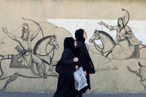 Dos mujeres con velo pasan por delante de un mural con una ilustración del poema épico persa Shahnama (Libro de los reyes), en el centro de Teherán, el 30 de enero de 2024