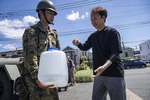 Un miembro de las Fuerzas de Autodefensa de Japón entrega un recipiente de agua a un hombre en un punto de distribución de agua