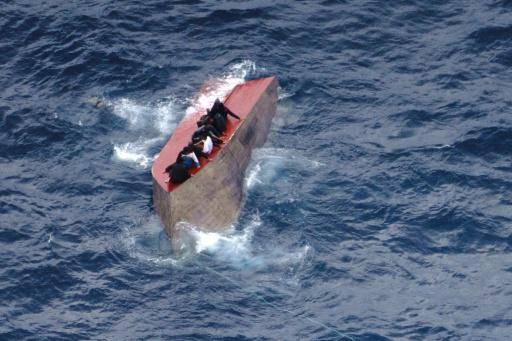 Unos migrantes se agarran al casco volcado de una embarcación naufragada frente a la costa de Libia el 4 de abril de 2026
