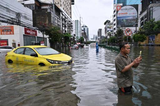 Un hombre graba un vídeo con su teléfono junto a un automóvil abandonado en una calle de Bangkok inundada tras las copiosas lluvias, el 26 de septiembre de 2026 en la capital tailandesa