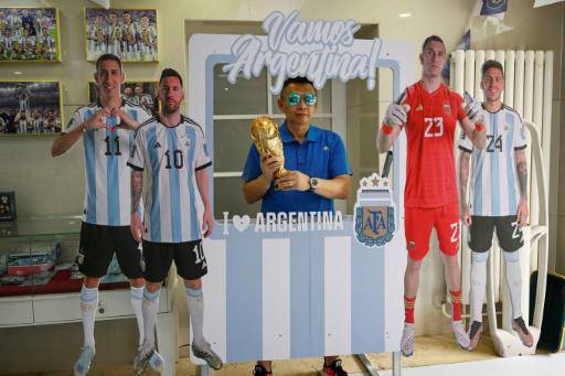 Un hombre posa para una fotografía con una réplica de la Copa del Mundo e imágenes de las estrellas de la selección de Argentina en una oficina de correos redecorada en Pekín, el 8 de junio de 2023