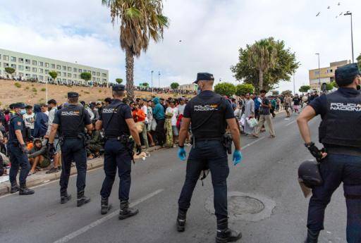 Agentes de la Policía Nacional montan guardia en una calle del barrio de Loma Colmenar ante un grupo de migrantes que aguardan a registrarse, el 31 de agosto de 2026 en la ciudad española de Ceuta, al norte de África