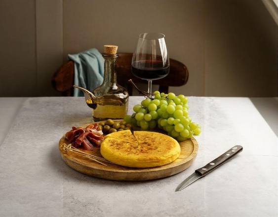 Freepik | Bodegón de tortilla española de patata junto con salami, aceitunas, uvas verdes y vino.