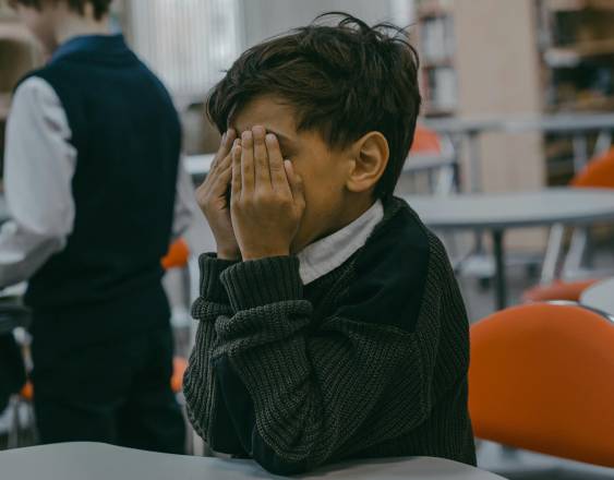 Pexels | Foto ilustrativa de un niño que sufre acoso escolar. Este se tapa el rostro.