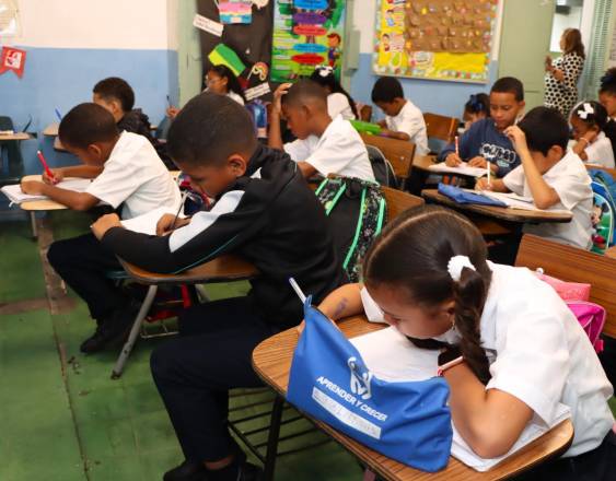 ML | Niños realizan tareas dentro de un plantel educativo supervisados por su maestra.