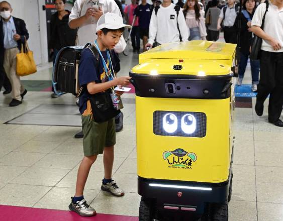 A young commuter puts waste into a mobile robotic trash bin being tested at the Shinjuku Station transport complex in Tokyo on September 18, 2026. The world's busiest railway station, located at the heart of Tokyo in Japan, is testing whether mobile robotic rubbish bins can ease the workload of sanitation workers, a rail operator representative said on September 18. (Photo by Toshifumi KITAMURA / AFP)