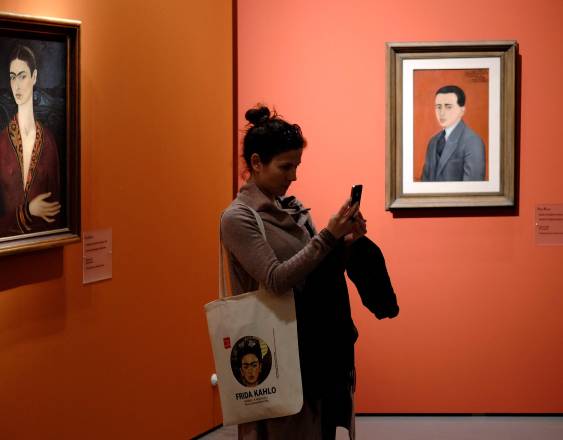 AFp | Un visitante toma fotos frente a “Autorretrato con vestido de terciopelo rojo” (izq.) de la artista mexicana Frida Kahlo durante la exposición en las Scuderie del Quirinale de Roma el 18 de marzo de 2014.