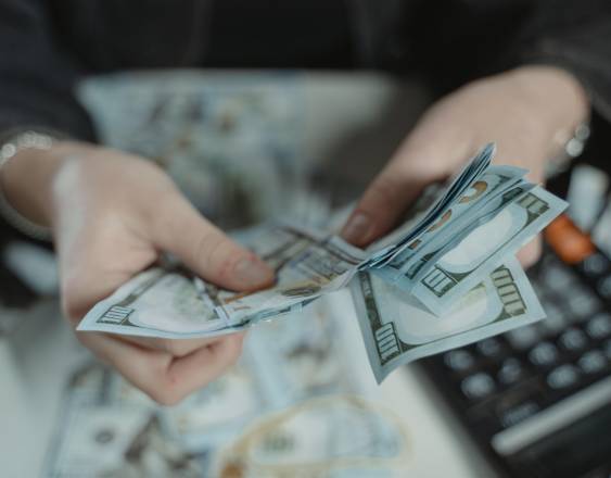 Pexels | Una persona contando dinero para realizar un pago en un banco.
