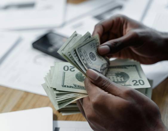 PEXELS | Una persona contando dinero sobre un escritorio. A su alrededor se observan documentos y una calculadora.