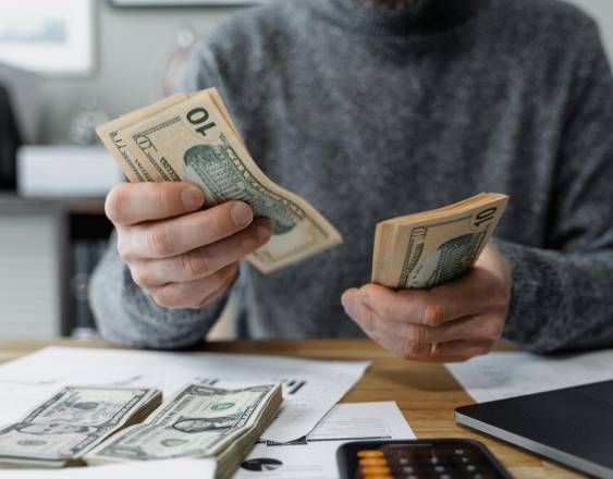 PEXELS | Una persona contando dinero para luego hacer el registro en su ordenador.