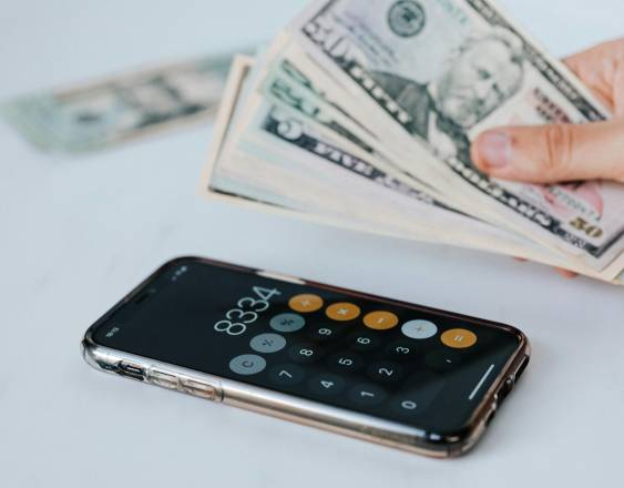 Pexels | Persona sostiene billetes, mientras utiliza la calculadora.