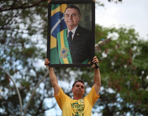 AFP | El candidato presidencial brasileño de derecha Flavio Bolsonaro sostiene una fotografía de su padre, el expresidente condenado Jair Bolsonaro.