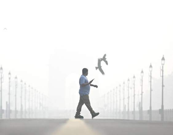 Un peatón camina entre el humo, cerca del India Gate.