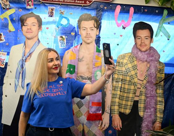 Una persona se toma una foto frente a fotografías de Harry Styles, dentro de la estación de tren en Holmes Chapel.