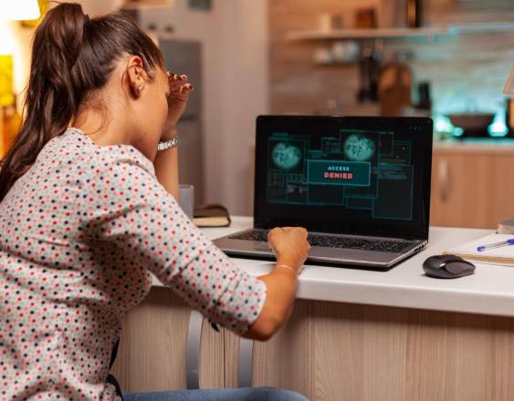 Una mujer sentada frente a una laptop que dice en la pantalla acceso denegado.