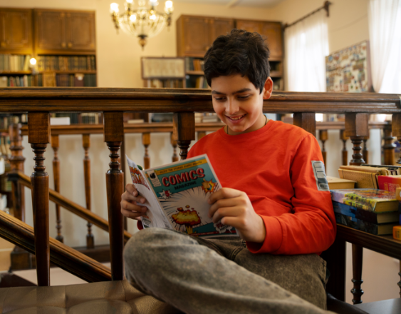 Freepik | Un niño sentado leyendo un comics en la biblioteca.