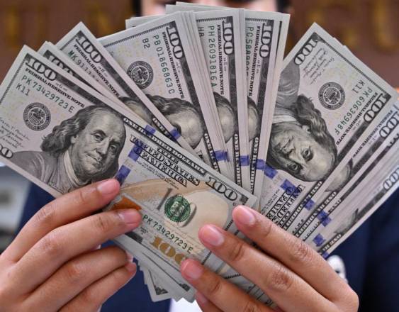 AFP | Una personas sostiene en sus manos billetes de cien dólares en un cambiador de dinero.