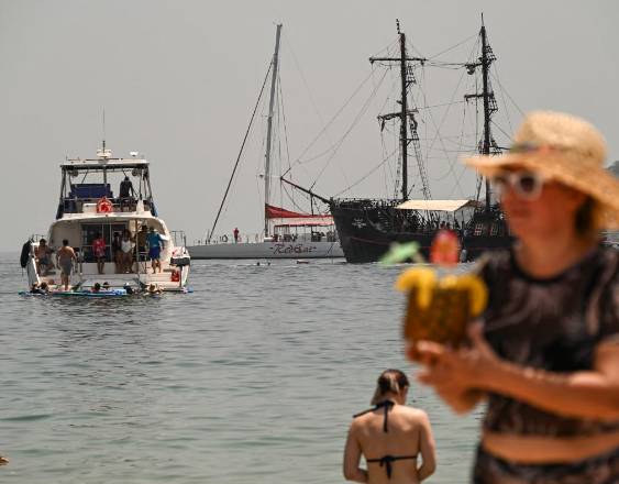 ML | Una mujer disfruta de una bebida en una playa donde también se observan otros turistas.