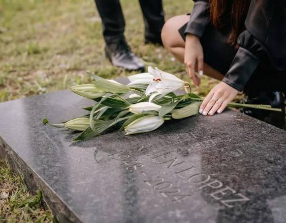 IA | Una persona en un cementerio colocando un ramo de orquídeas sobre la tumba de un familiar.