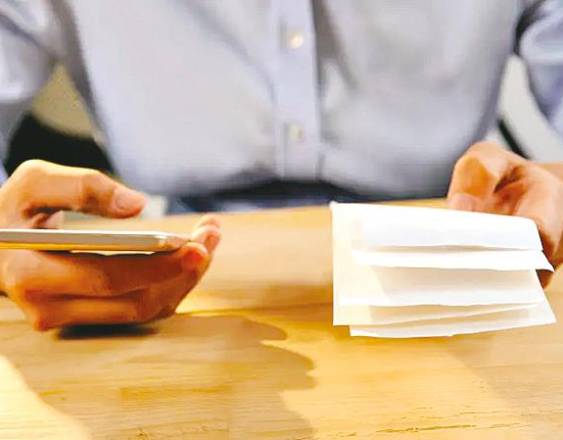 PEXELS | Una persona con un celular y unas facturas en la mano.