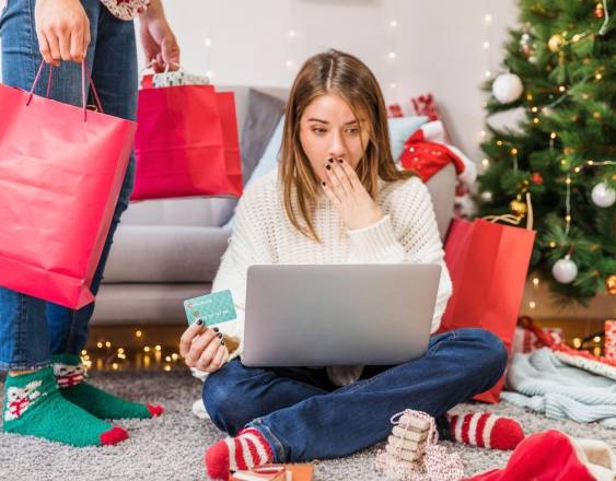 Freepik | Una mujer en temporada de Navidad sentada en el piso de su casa realizando compras en sitios digitales desde su computadora.