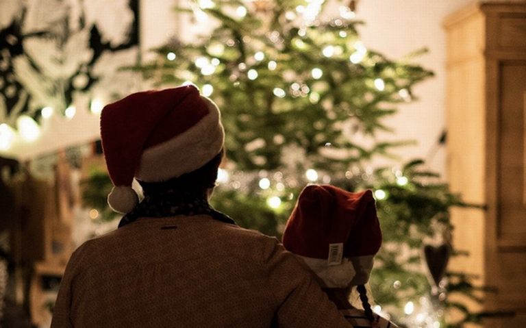 ML | Una familia con gorros navideños mirando las luces en el árbol de navidad en la sala de su hogar.