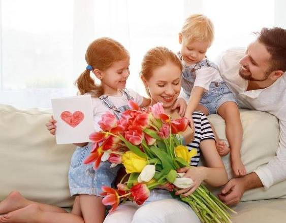 Generada con IA | Una madre recibe flores y cartas de su esposo y de sus dos hijos en el Día de la Madre.