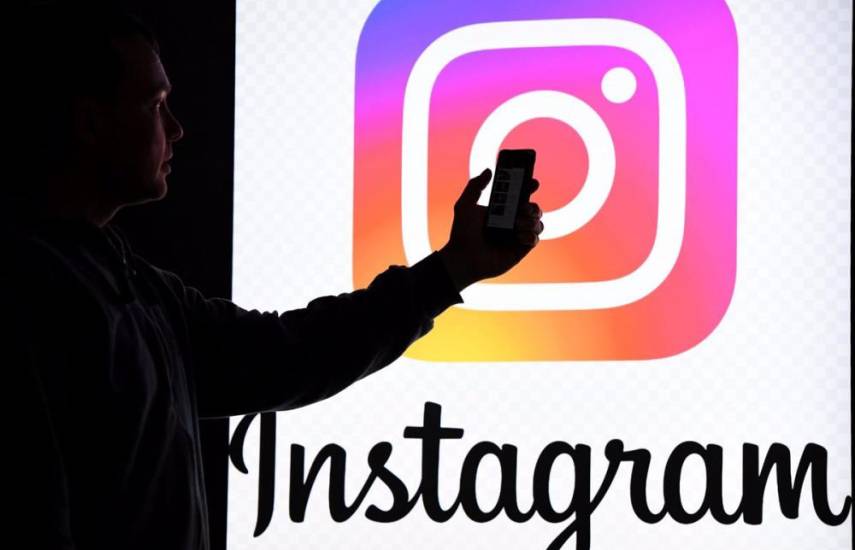 Una persona sostiene un teléfono inteligente frente a un monitor con el logo de la red social Instagram.