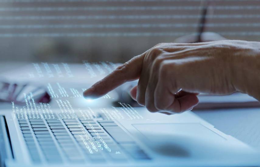 ML | Una persona escribe en el teclado de una laptop, mientras se reflejan diversos códigos.