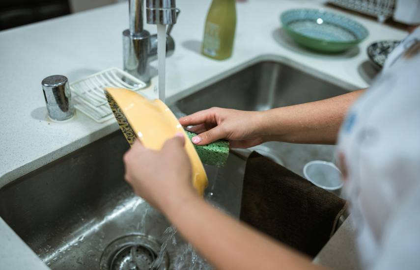 PEXELS | Una mujer fregando con agua saliendo del grifo.
