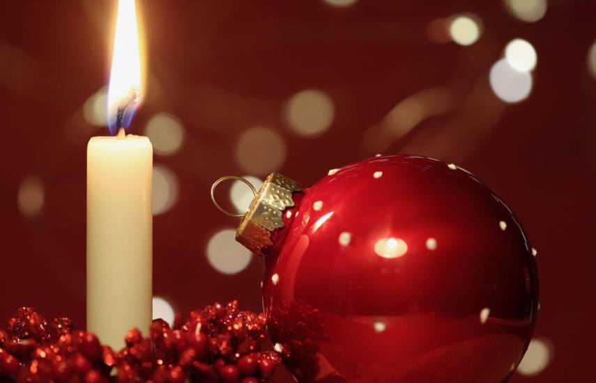 Pixabay | Una vela encendida, al lado de la esfera roja utilizada en las decoraciones de Navidad.
