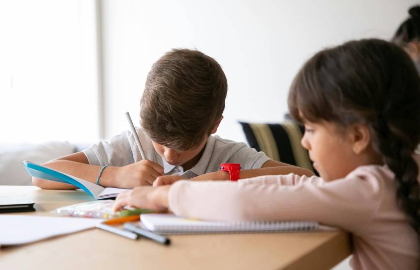 PEXELS | Dos niños haciendo tarea sobre un escritorio en casa.