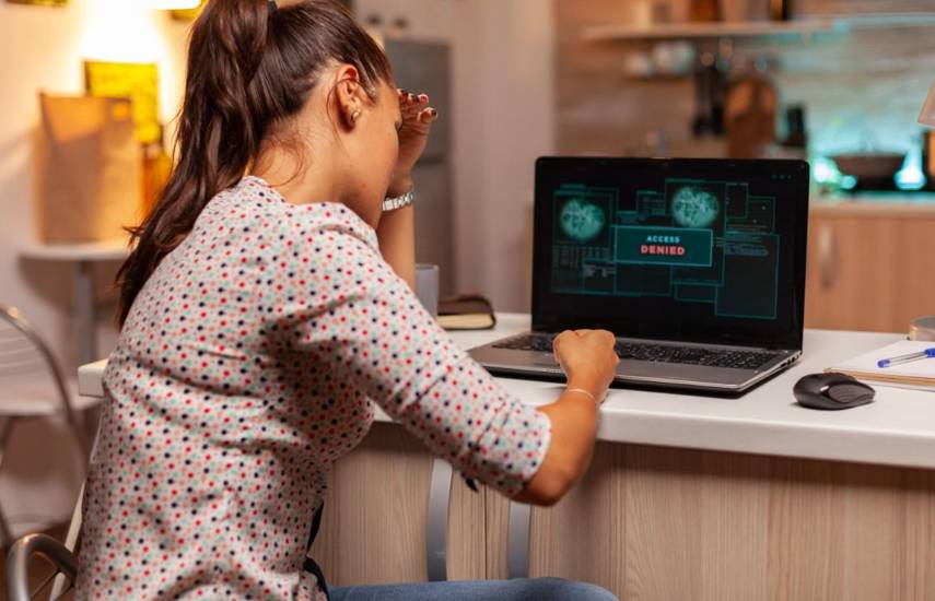 Una mujer sentada frente a una laptop que dice en la pantalla acceso denegado.