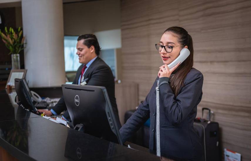 Pixabay | Dos recepcionistas trabajando en un hotel. El hombre se prepara para recibir a un grupo de turistas. Mientras, la mujer atiende una llamada para realizar reservas próximas en el hospedaje.