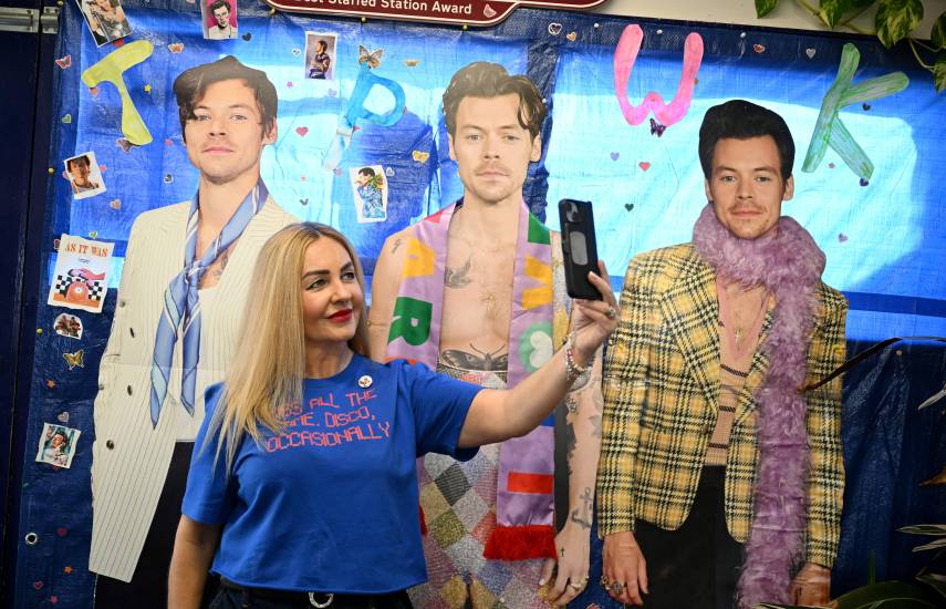 Una persona se toma una foto frente a fotografías de Harry Styles, dentro de la estación de tren en Holmes Chapel.