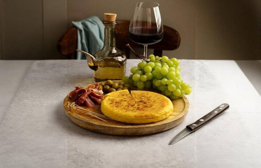 Freepik | Bodegón de tortilla española de patata junto con salami, aceitunas, uvas verdes y vino.